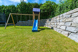 Haus Urmmel Außenansicht Garten mit Steinmauer und Rutsche mit Schaukeln für Kinder
