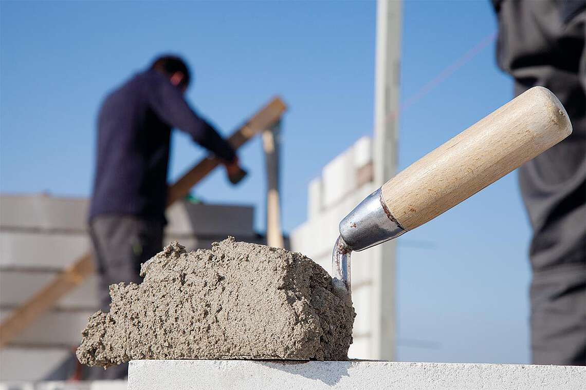 Maurerkelle befüllt mit Zement für den Massivhausbau durch Maurer und Betonbauer